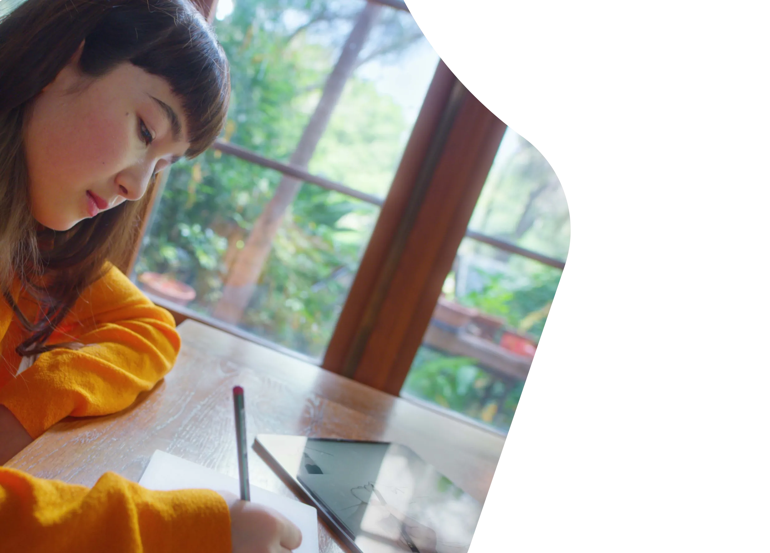 A young woman drawing in a sketchbook next to an iPad